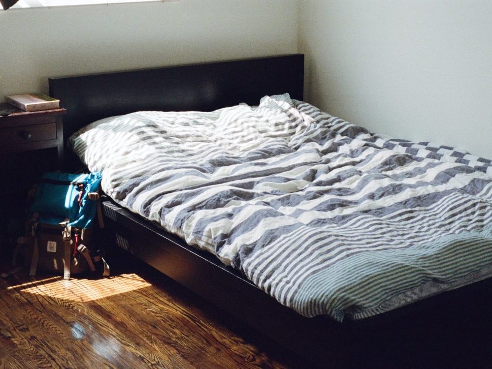 black wooden bed framed and white and gray striped bedspread